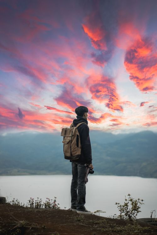 Free A lone backpacker stands on a mountain top in Indonesia, watching a vibrant sunset sky. Adventure awaits. Stock Photo