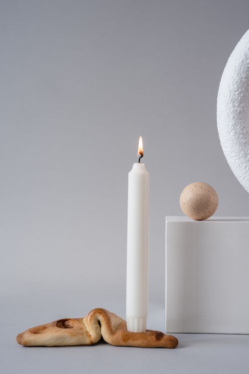 Free A minimalist still life featuring a lit candle, a bread piece, and a wooden ball on a gray background. Stock Photo