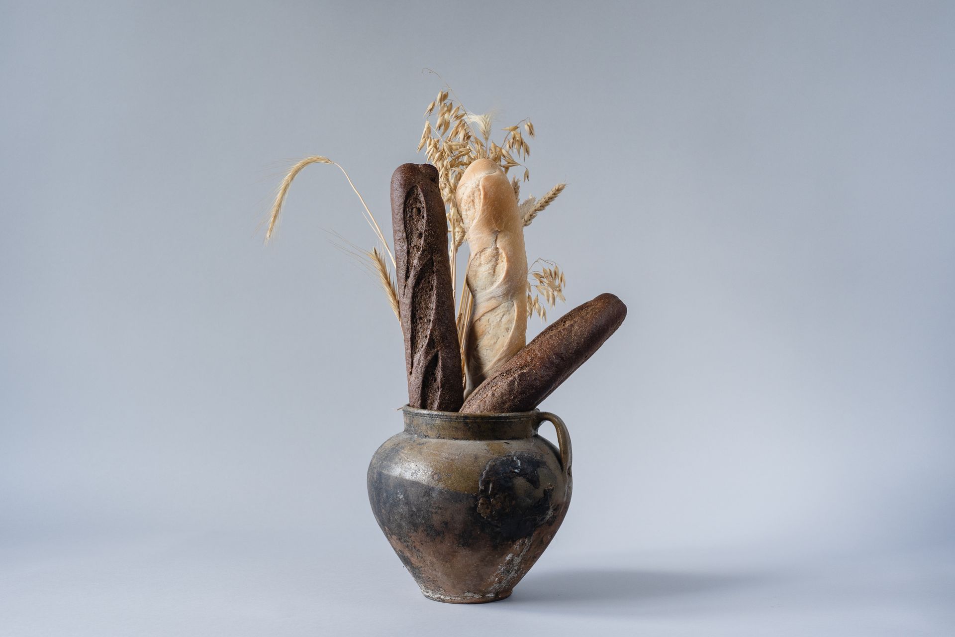 Artistic composition of baguettes in a rustic ceramic vase with spikelets on a gray background.
