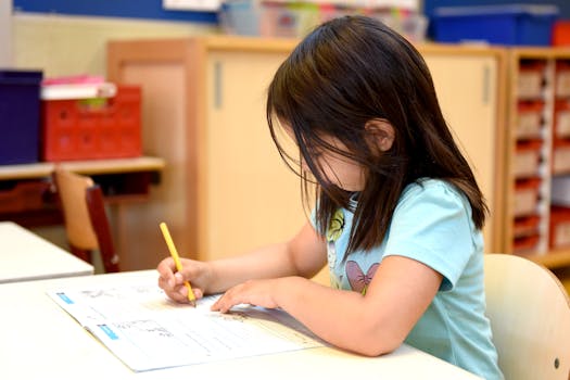 Young girl in school classroom focused on writing with a pencil at her desk.