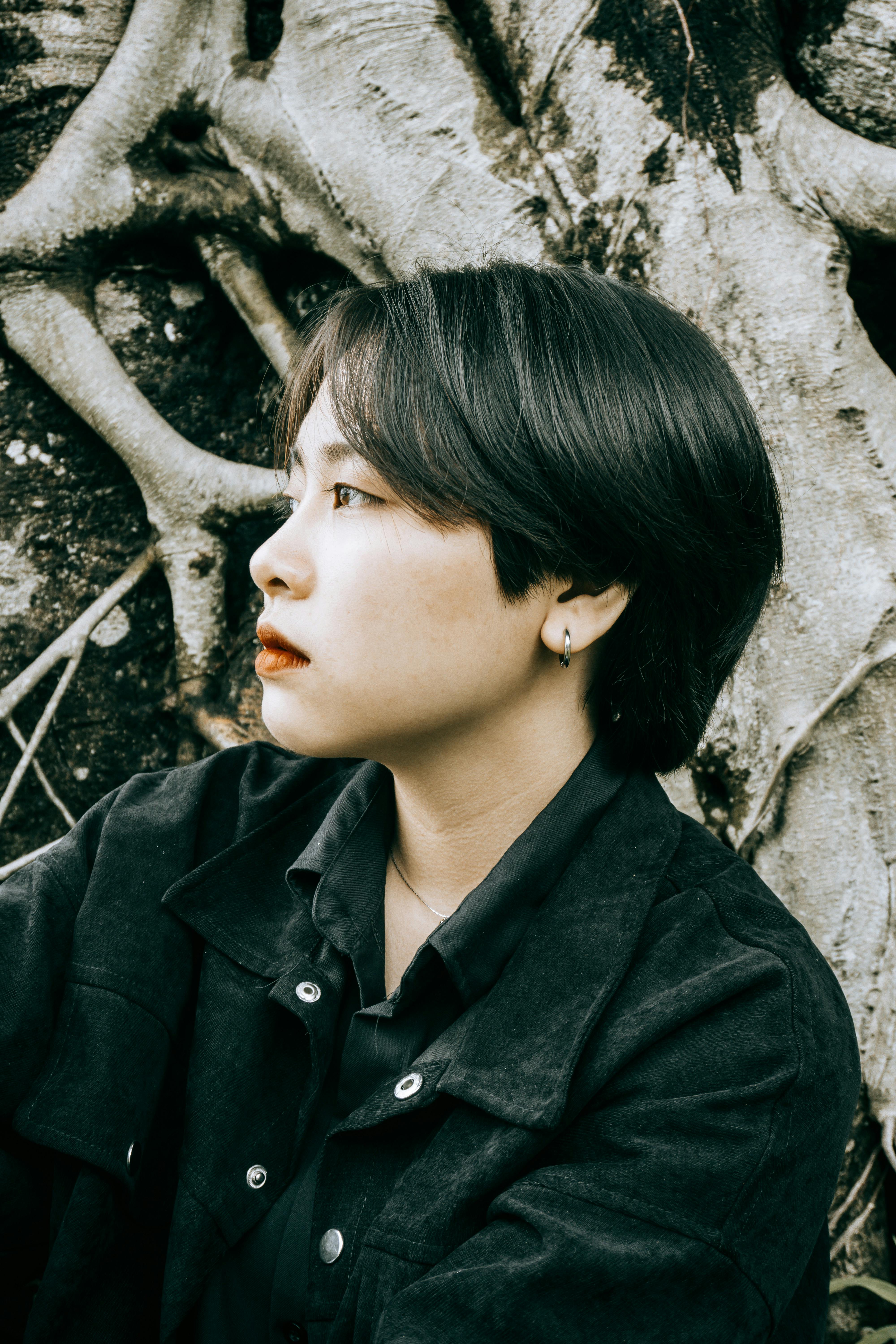 A fashionable woman with short hair in a black jacket, looking contemplative against a textured background.