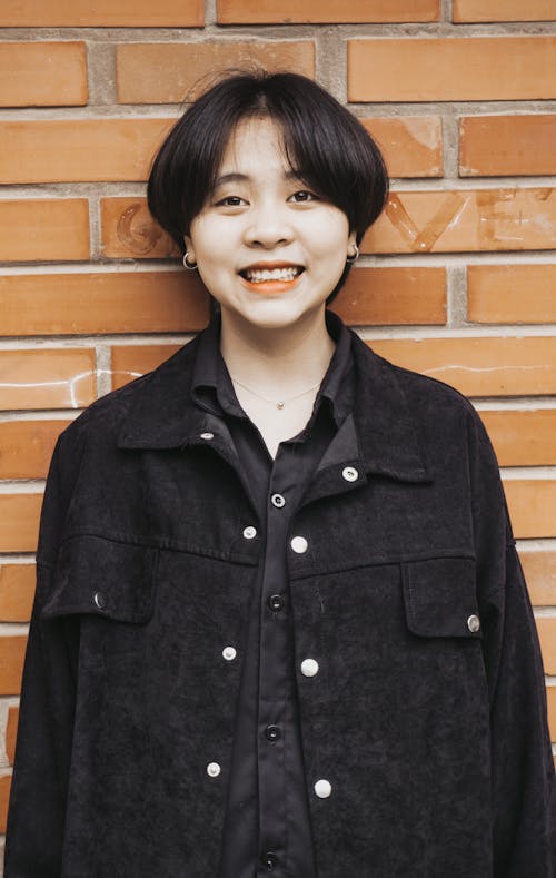 Woman in Black Button Up Jacket Standing Beside Brown Brick Wall