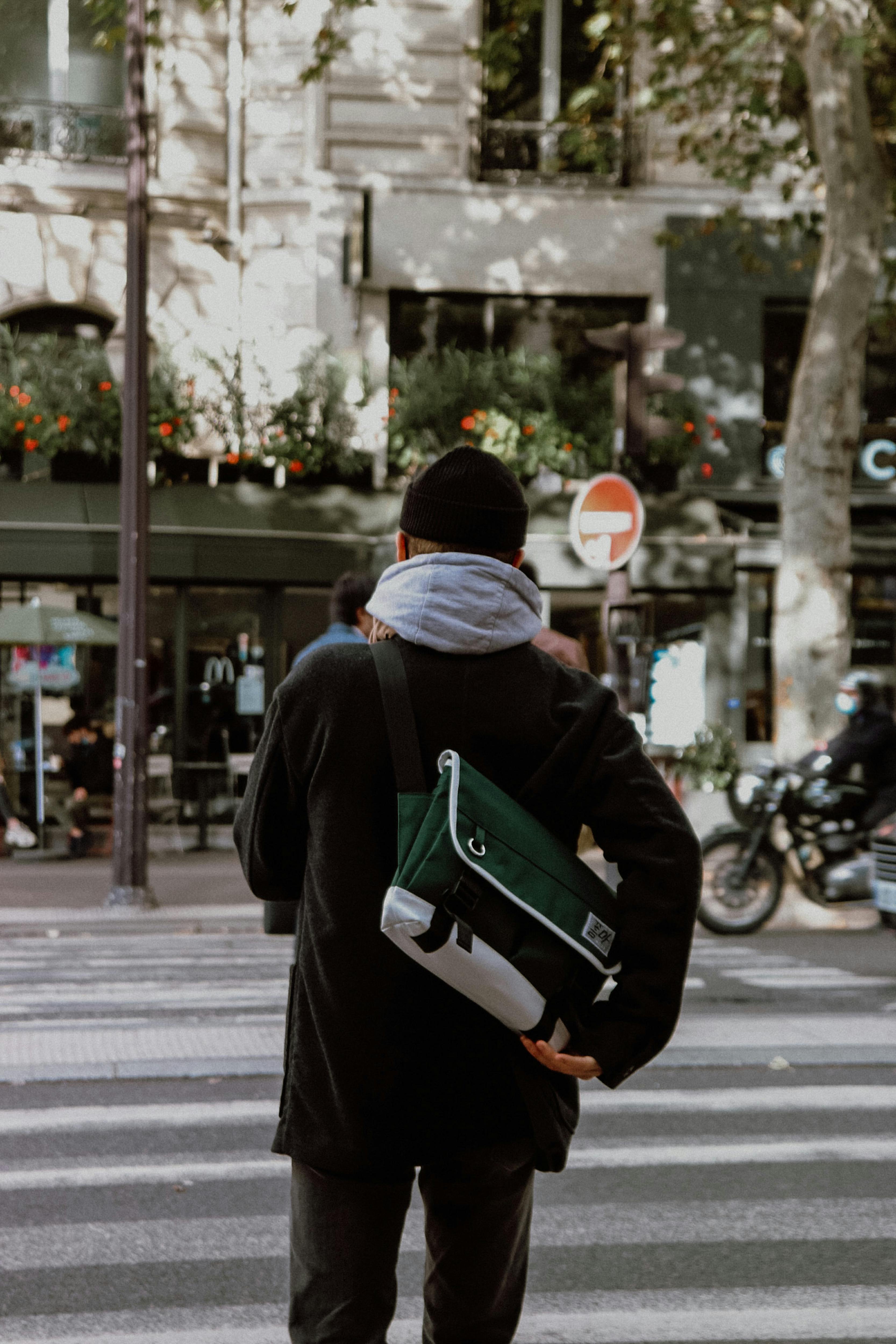 Back view of a man crossing a city street with a backpack and knit hat.