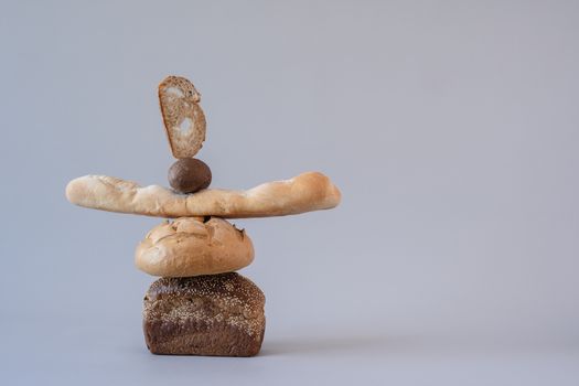 Artistic arrangement of diverse bread types balancing against a gray backdrop, showcasing still life photography.