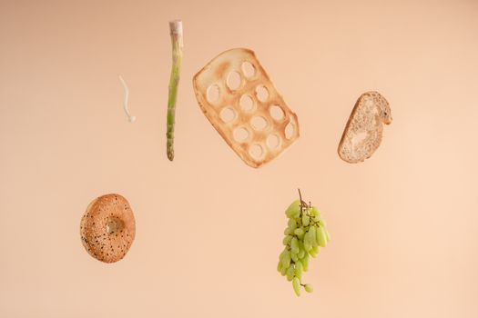 Artistic arrangement of floating bread, grape cluster, and vegetables on a peach background.