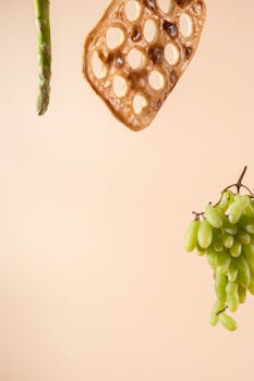 Artistic arrangement of green grapes, asparagus, and crisp bread on a peach background.