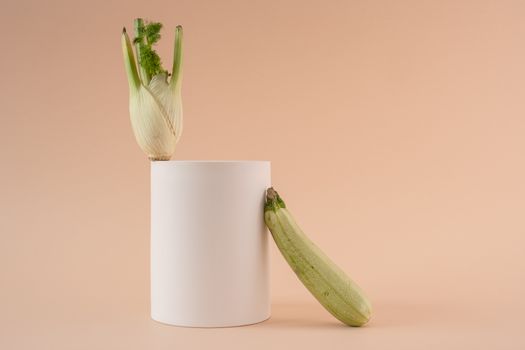 A minimalist still life composition featuring fennel and zucchini against a warm orange background.