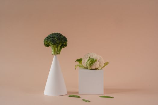 A minimalist food photography capturing broccoli and cauliflower on geometric shapes with a beige background.