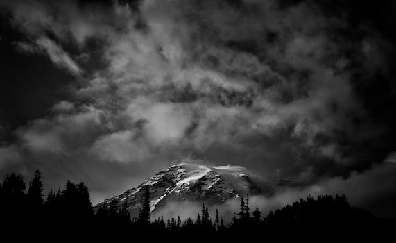 A stunning black and white photograph of Mount Rainier with dramatic clouds overhead.