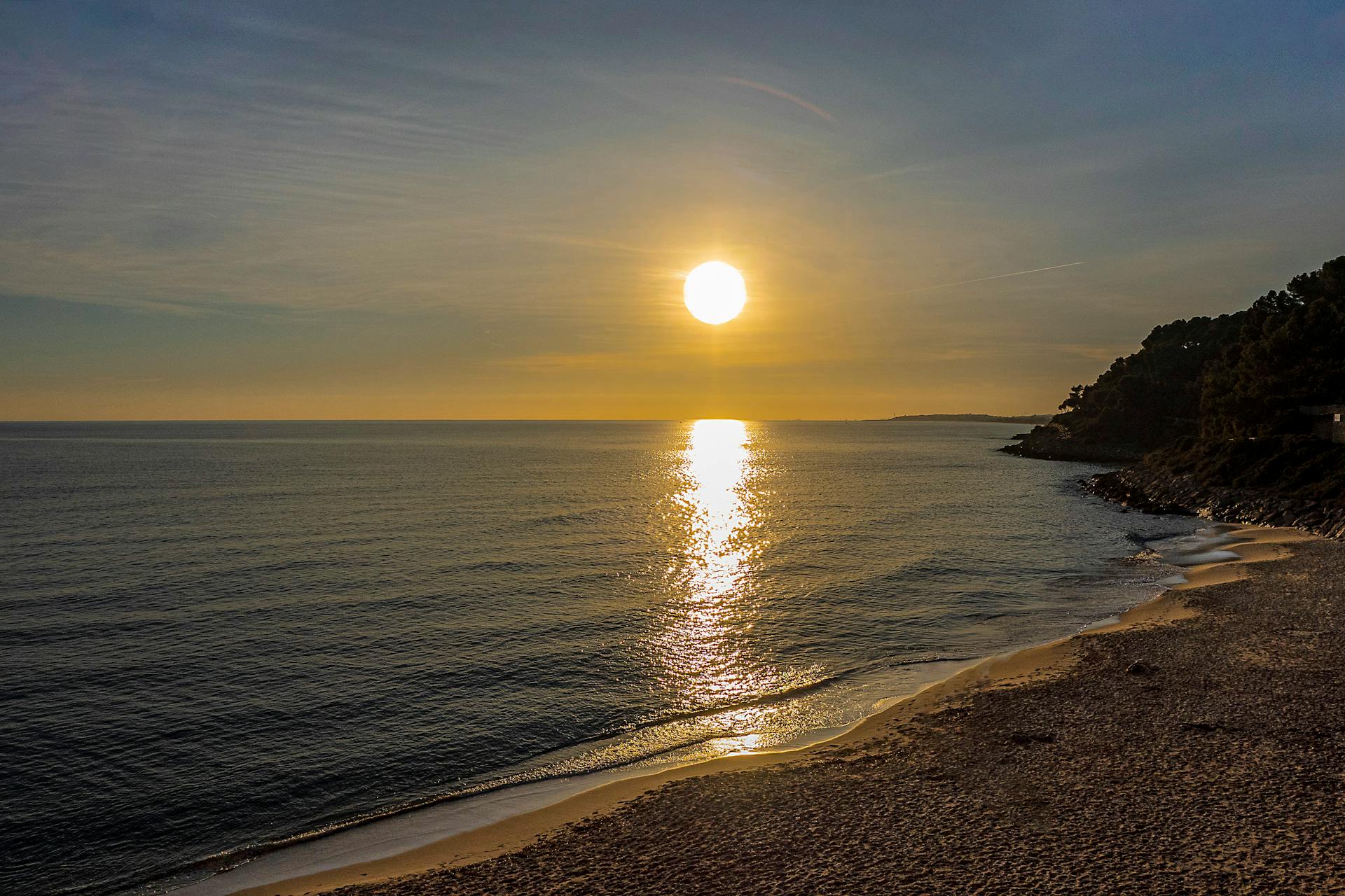 Sunset casts golden hues over a peaceful Catalonia beach, capturing serene coastal beauty.