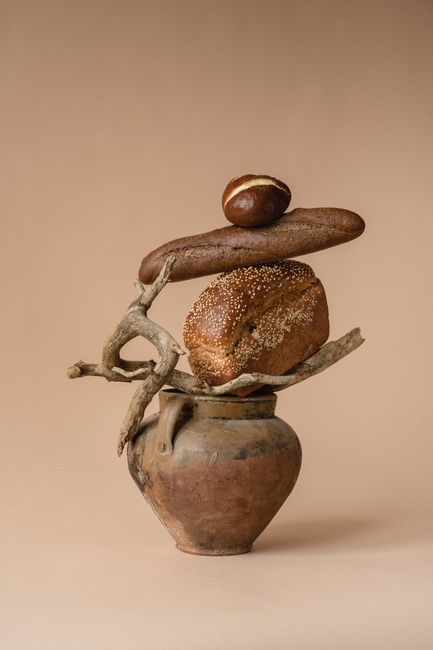 A creative composition of artisan bread atop pottery against a beige background.