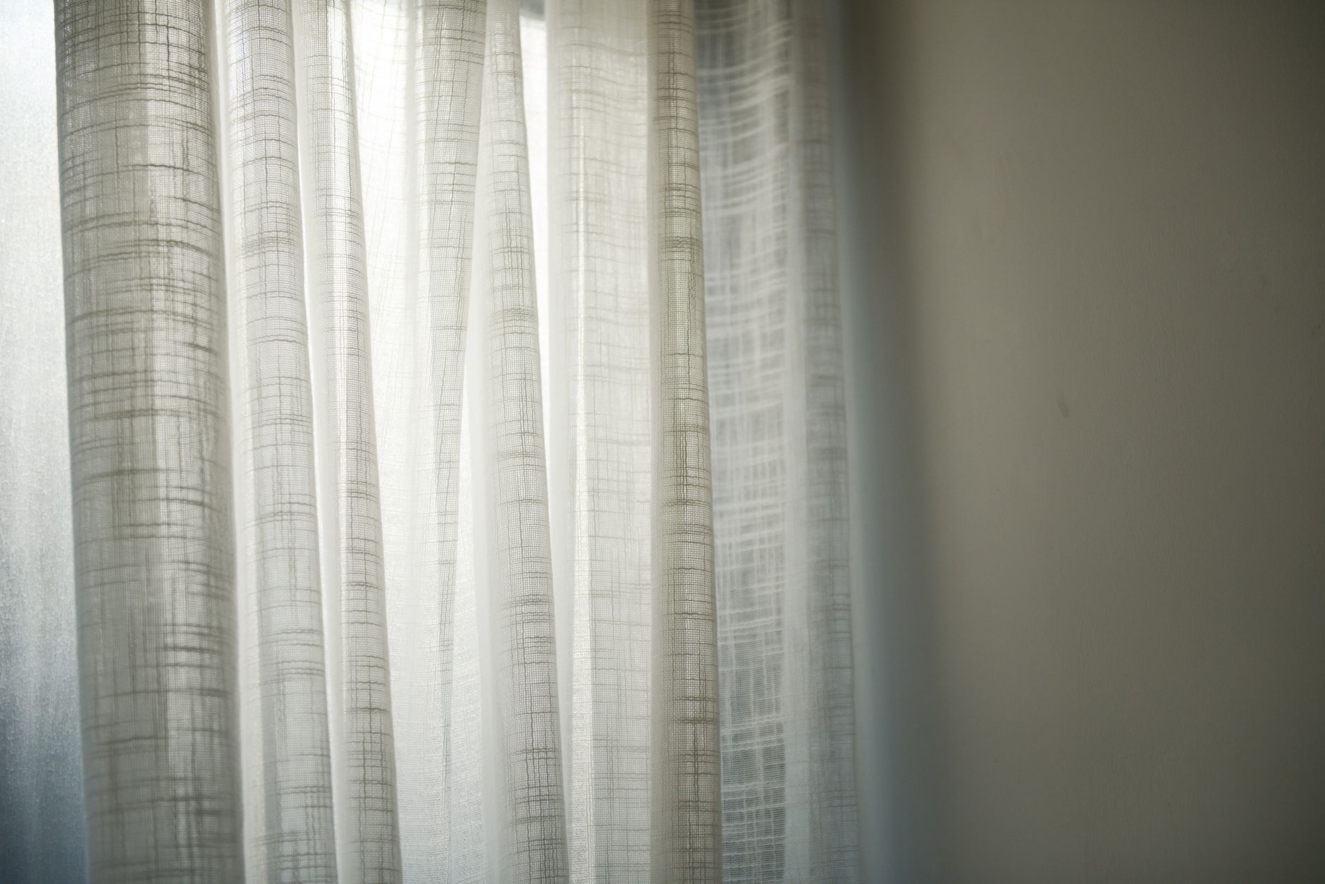 窗簾選購不後悔流程:先評需求、後配風格、再挑材質 Sheer white curtains gently lit by daylight create subtle shadows on the wall.