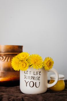Yellow dandelions placed in light mug against wall