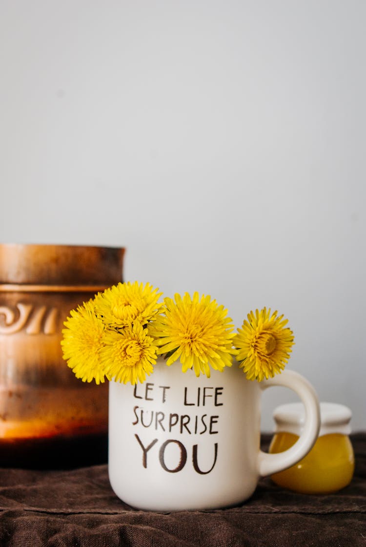 Yellow Dandelions Placed In Light Mug Against Wall