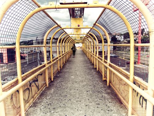 Free A modern pedestrian bridge with yellow wire mesh and a lone walker, creating a striking urban design. Stock Photo