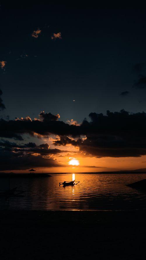 Free A tranquil Bali sunrise with a silhouetted boat on the calm sea, capturing the golden hour's beauty. Stock Photo