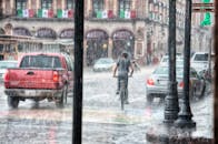 在墨西哥莫雷利亚的街景中，一名骑自行车的人正冒雨前行