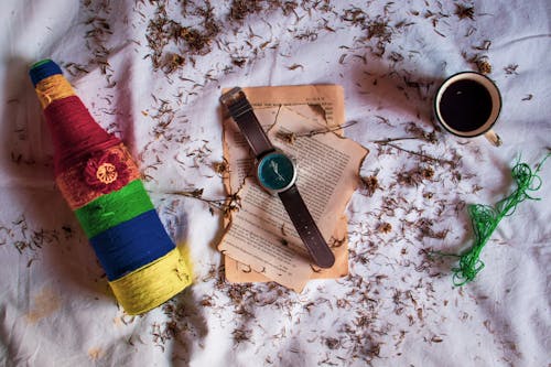 Top view of vintage wristwatch placed on pages of old book on table with colorful decorated bottle and cup of hot drink