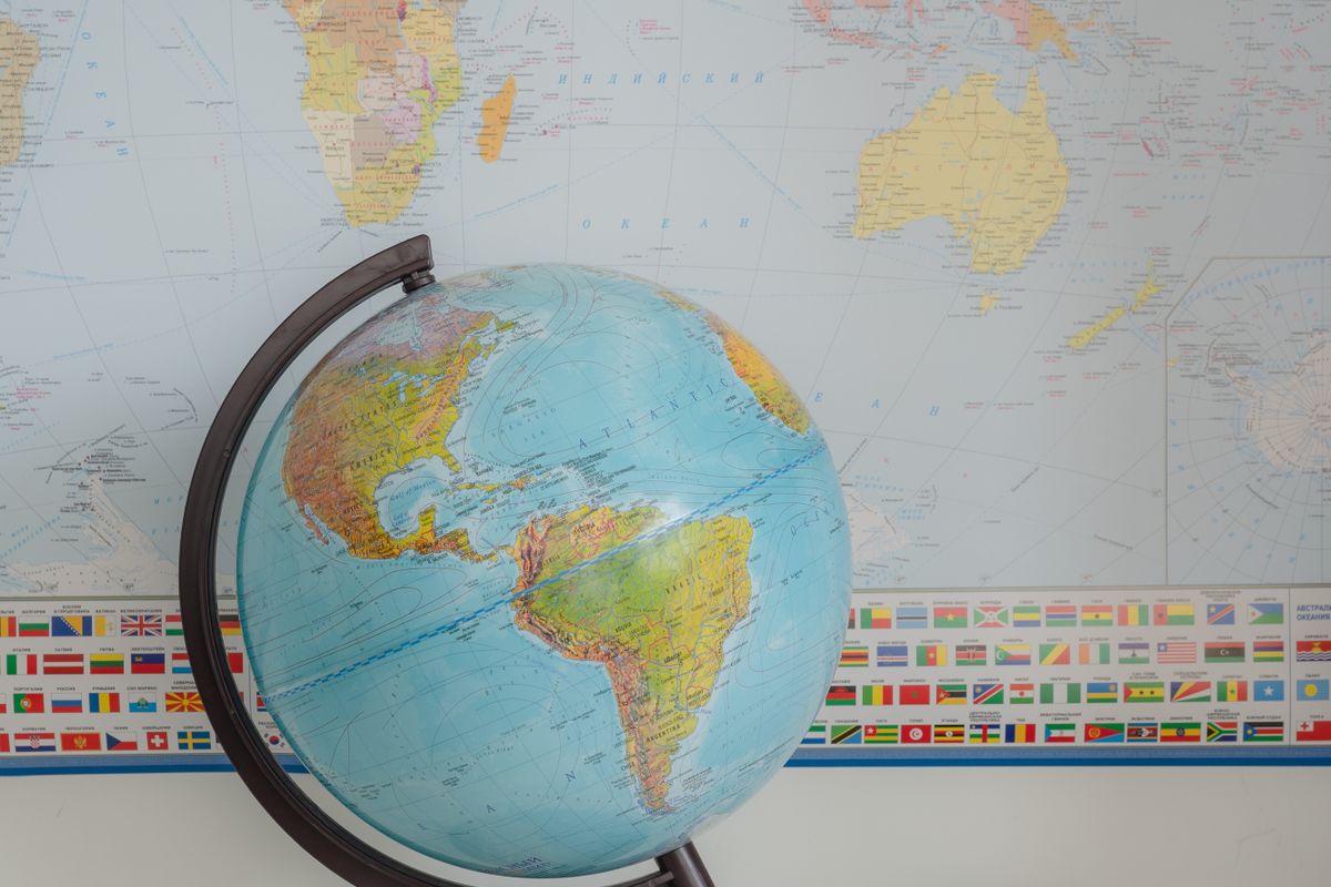 Desk globe in front of a wall world map with a row of national flags along its edge