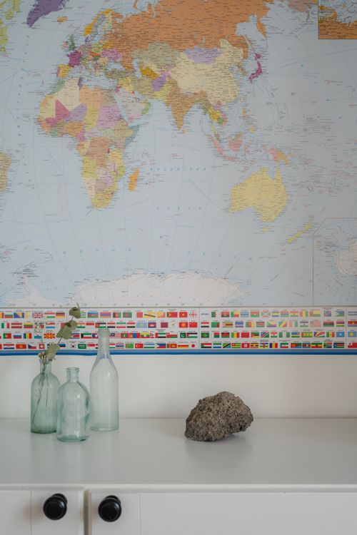 Free Glass bottles with a world map backdrop creating a travel-themed display on a modern white shelf. Stock Photo
