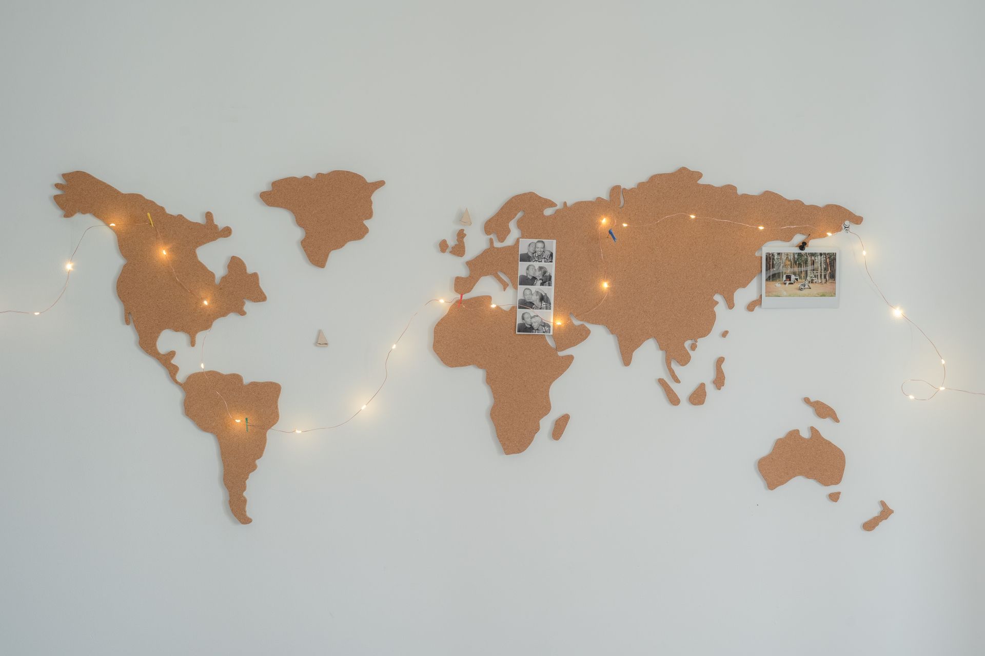 Cork world map wall decor with fairy lights and pinned photographs on a white background.