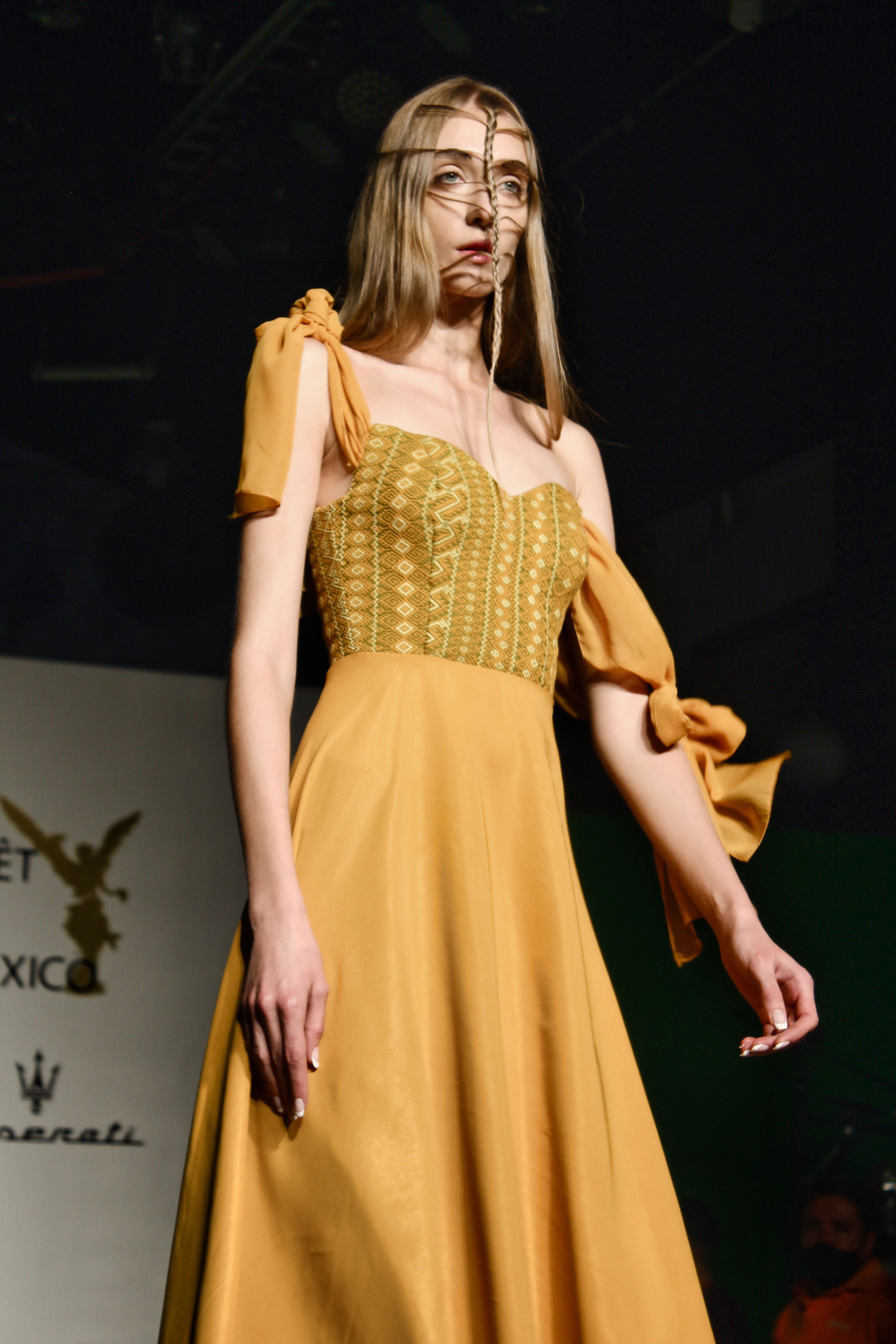 Modelo com um vestido amarelo estiloso desfilando na passarela de um desfile de moda na Cidade do México.