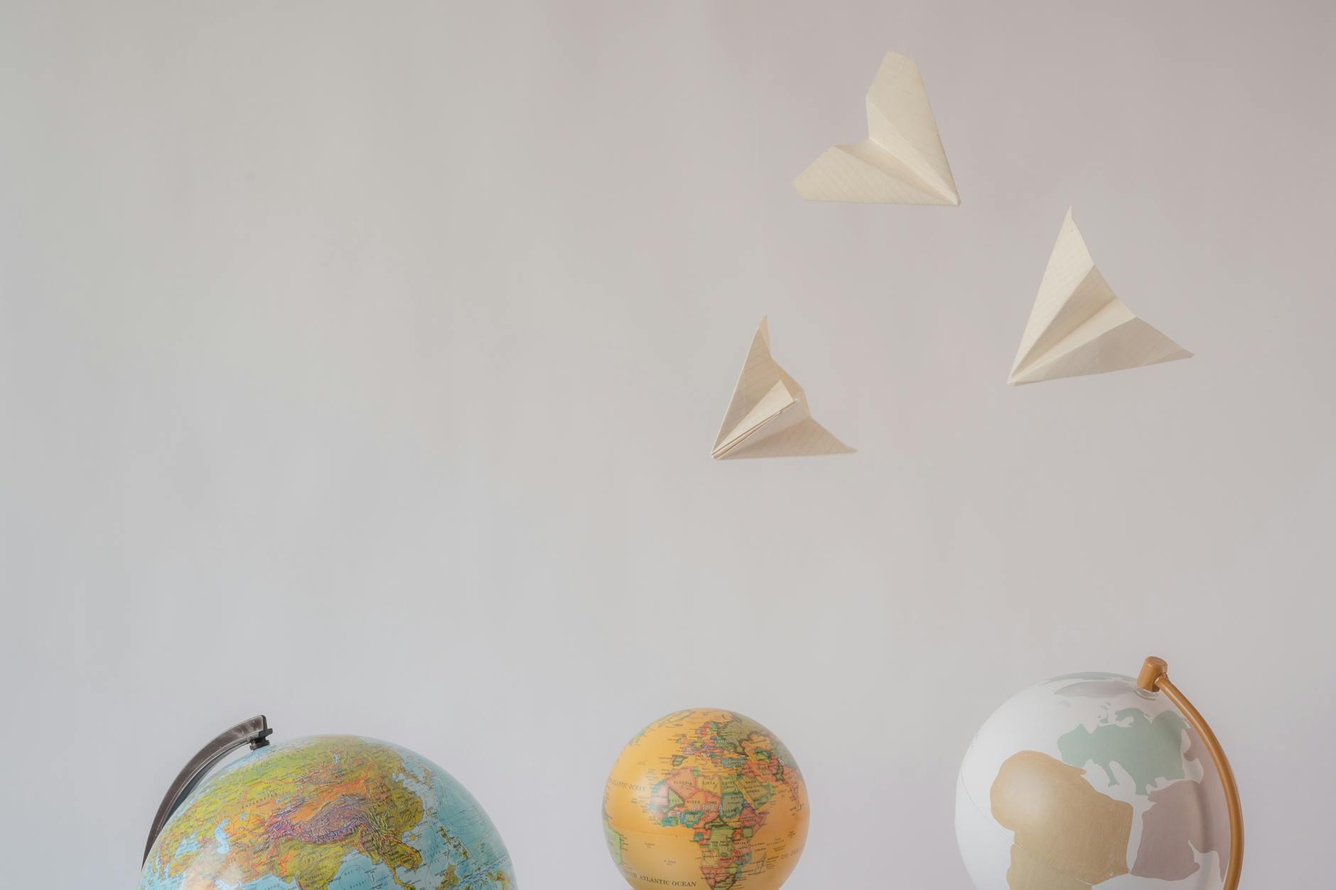 Paper airplanes fly over colorful globes, symbolizing travel and exploration on a white background.