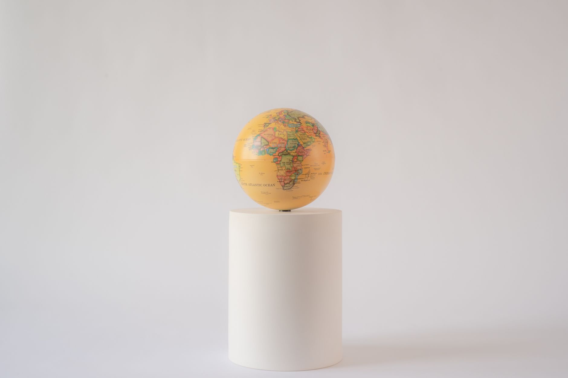 A minimalist photo of a world globe balanced on a white cylindrical pedestal.