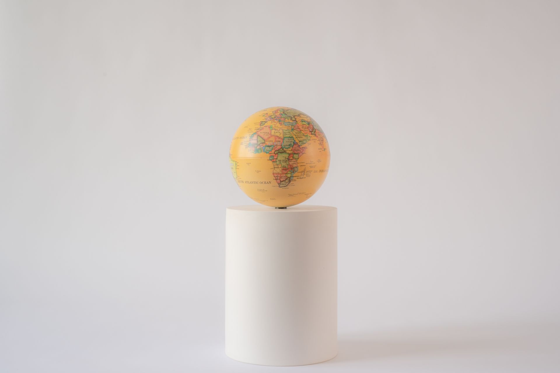 A minimalist photo of a world globe balanced on a white cylindrical pedestal.