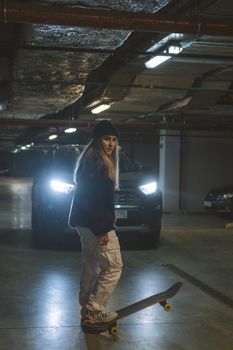 Young woman skateboarding in a dimly lit underground parking garage at night.