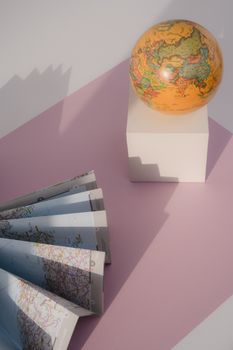 A globe and a folded paper map on a pink surface with shadows creating a conceptual travel theme. 7634858