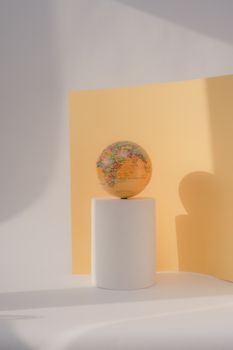 A colorful globe on a pedestal against a geometric yellow backdrop showcasing a minimalist still life. 7634889