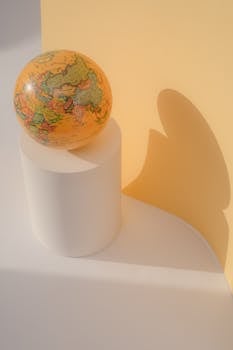 A colorful world globe casts a playful shadow on a yellow background, creating a minimalist aesthetic.