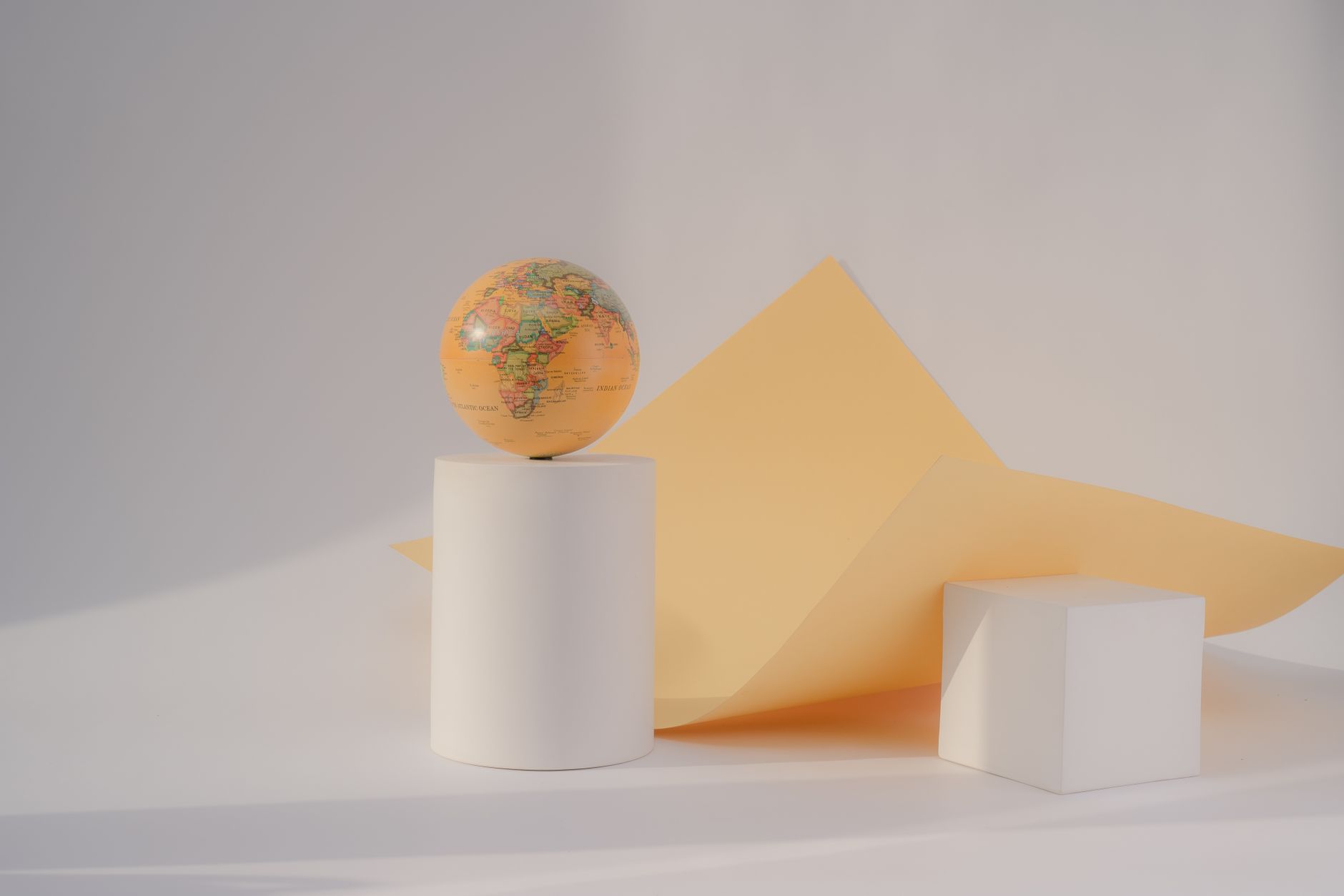 Conceptual still life featuring a globe on geometric white shapes with orange paper.
