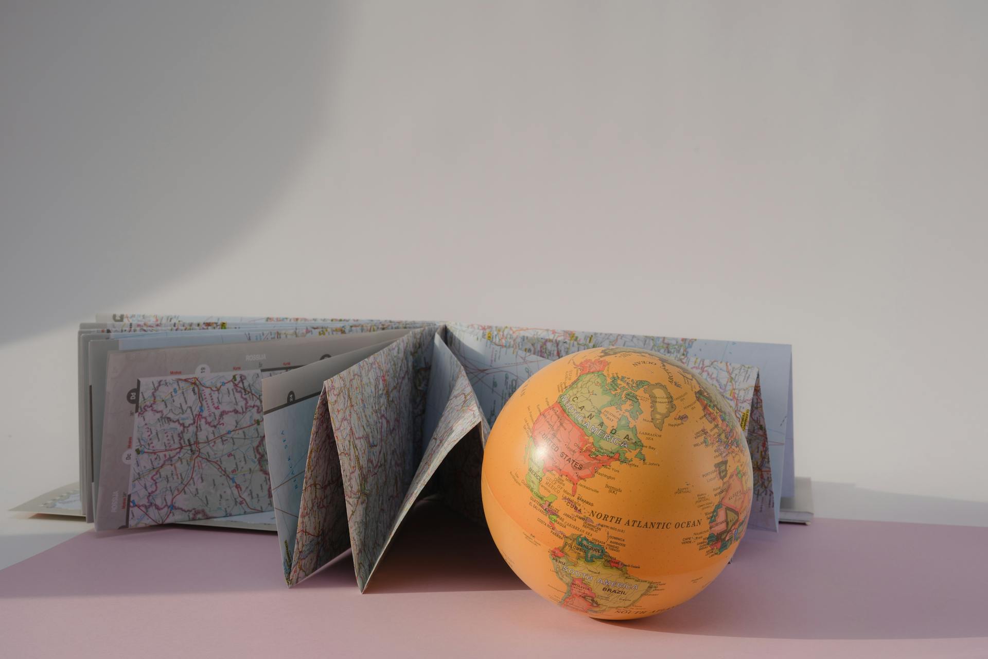 Vibrant globe and folded map in a minimal still life setting, ideal for travel and geography themes.