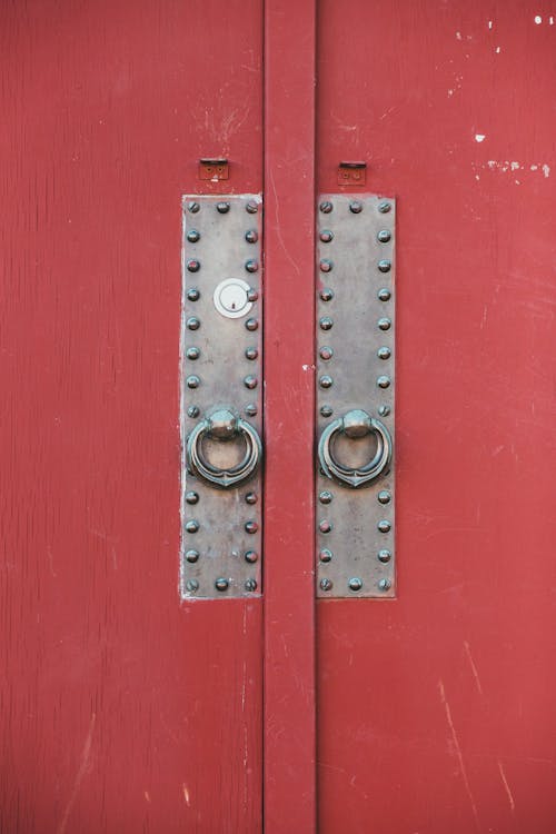 Exterior of building with closed bright red shabby door with metal handles on street in daylight