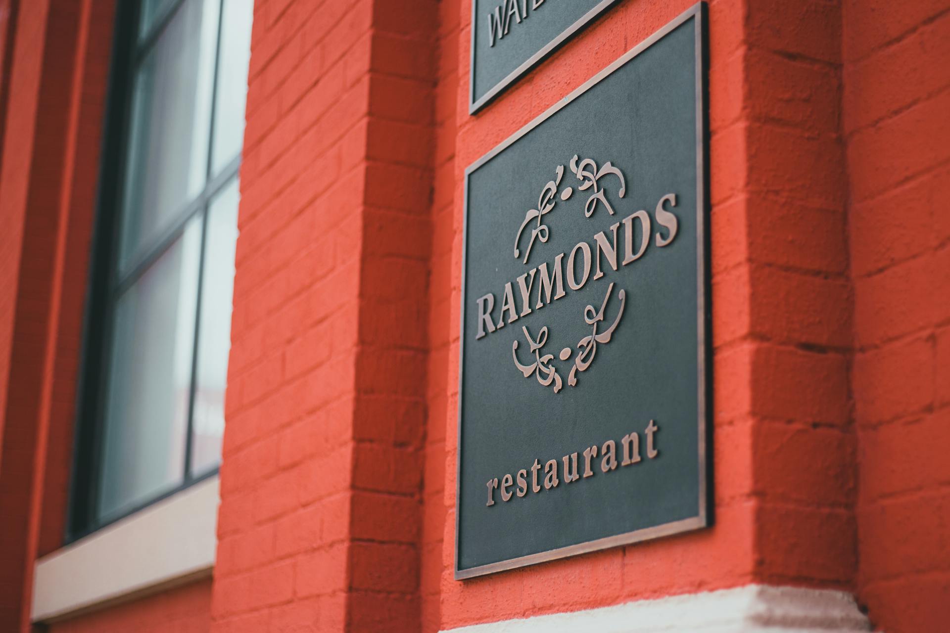 Close-up of Raymonds restaurant sign on vibrant red brick exterior in daylight.