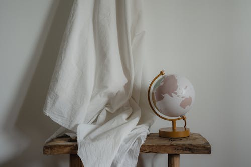 A Globe Desk Lamp on the Wooden Table Near the White Textile