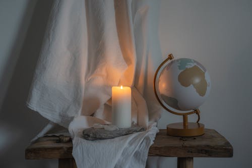 
A Lighted Candle beside a Globe on a Wooden Bench