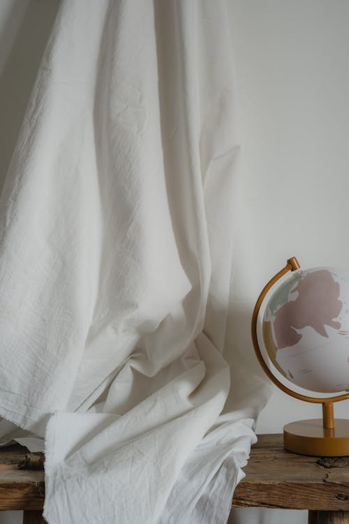 A Globe Lamp on the Wooden Desk with a White Textile Backdrop