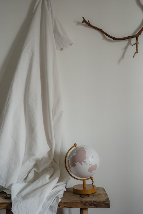 A Globe on the Wooden Bench Near the Hanging Textile and Branch