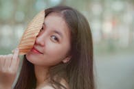 一位年轻女子在自然的户外环境中，微笑着与一片干树叶开玩笑地摆姿势