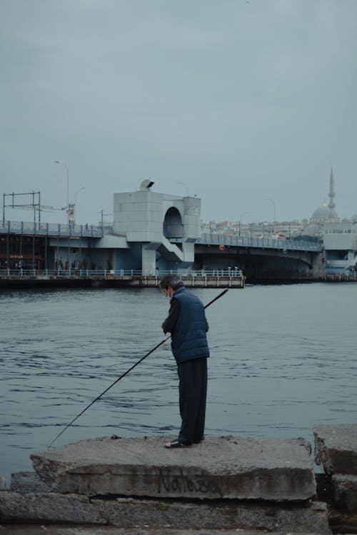 Faceless male with fishing rod near river and bridge