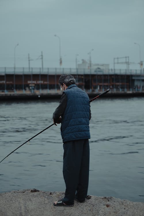 Unrecognizable fisherman with rod near river and bridge