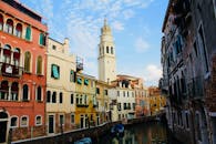 沿着威尼斯运河探索，两侧是历史建筑和蓝天映衬下的教堂塔楼