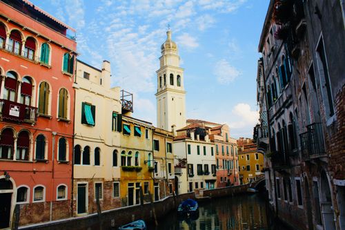 Free Explore Venetian canals flanked by historic buildings and a church tower under a blue sky. Stock Photo