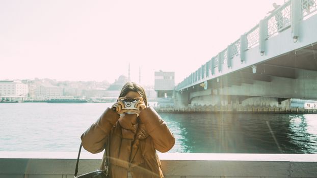 Woman takes photo near Galata Bridge, Istanbul with serene cityscape in background.