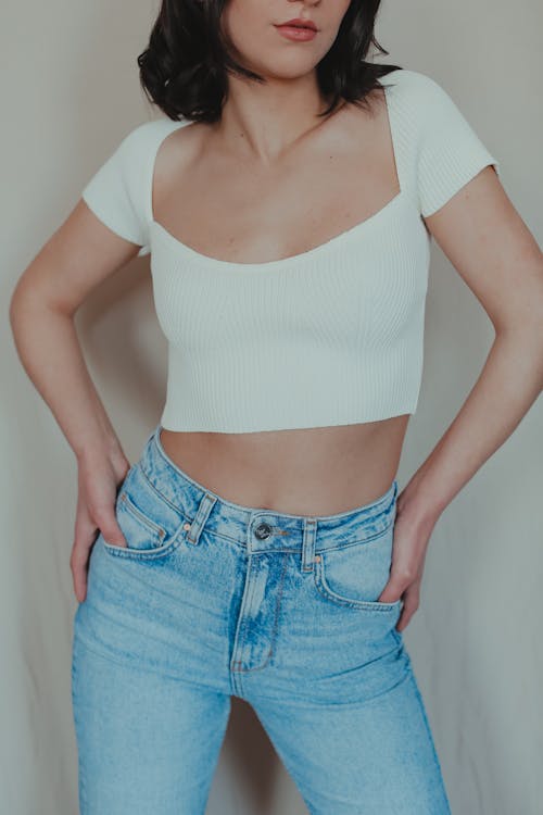 Woman in White Crop Top and Denim Jeans with Her Thumbs in Her Pockets