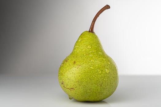 Vibrant green pear with water droplets on a neutral background, highlighting freshness.