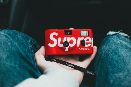 From above of crop faceless person in ripped jeans with red vintage camera with white inscription and strap in hand